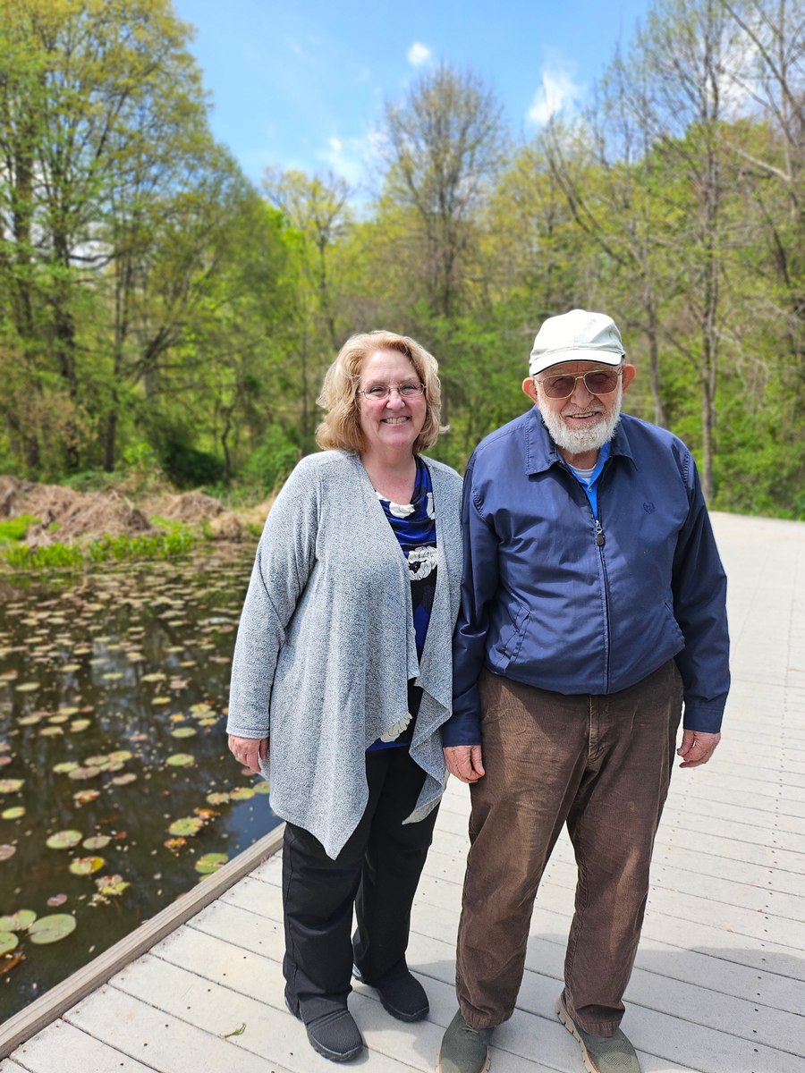 Two people smiling beside a pond on a wooden boardwalk